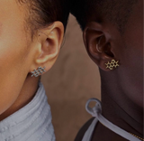 Close-up of two people wearing molecular structure earrings. The person on the left sports melanin structure earrings in silver with a white top, while the person on the right has gold ones with a white halter top.