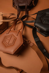 Hexagonal handbags in beige, brown, and black with embossed geometric logos are arranged on a brown surface. Each bag features gold-colored hardware and is paired with a matching strap, elegantly mirroring the intricate allure of chemical structure jewelry.