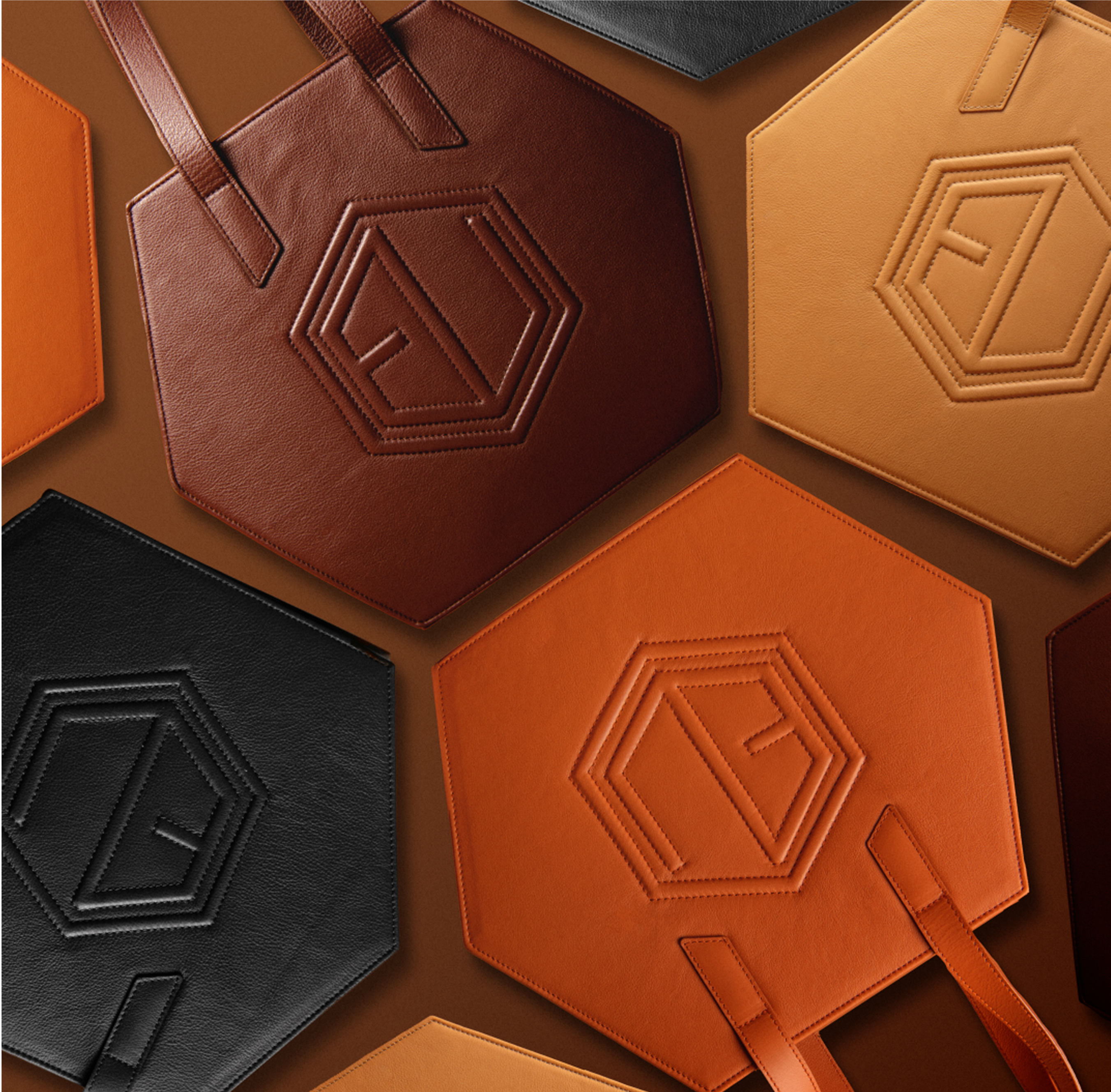 Geometric HEX Bags in shades of brown, orange, and black with embossed logos are arranged on a brown background. Featuring premium hardware and luxe allure leather, the bags hexagonal shapes contrast stylishly, showcasing a modern design.