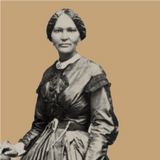 Historic photograph of a woman with short hair wearing a patterned dress, adjusting fabric on a mannequin in an elegant shop. The image, rich in eumelanin contrasts, is black and white against a solid brown background.