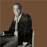 A person in a vintage photograph sits on a chair, wearing a dark jacket, white shirt, and tie. The solid brown background accents the image’s classic, monochromatic look. Subtle eumelanin hues add depth to the timeless capture.