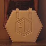 Tan hexagonal handbag with double handles and embossed geometric logo, crafted in luxe allure leather. Background is a matching shade.