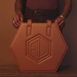 The Hexagonal caramel-colored handbag, known as the HEX Bag, exudes luxe allure with its embossed geometric pattern and premium hardware. Two sturdy handles complement the elegant design.