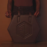 The HEX Bag in hexagonal dark chocolate brown leather exudes luxe allure with two straps and premium hardware. A bold embossed logo graces the center, with a matching background.